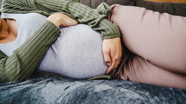 ilustrasi kontraksi Tired stressed pregnant woman sitting on a couch and holding her belly