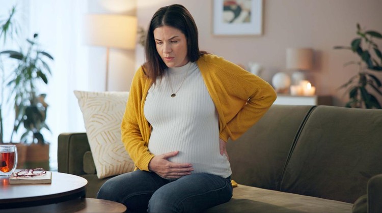 Tired stressed pregnant woman sitting on a couch and holding her belly