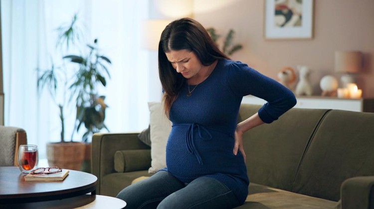 Tired stressed pregnant woman sitting on a couch and holding her belly