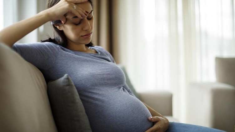 Tired stressed pregnant woman sitting on a couch and holding her belly
