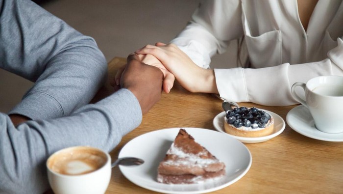 Interracial couple holding hands sit at cafe table, african black man and white woman in love enjoy date in coffee house concept, romantic biracial lovers meet in public place together, close up view