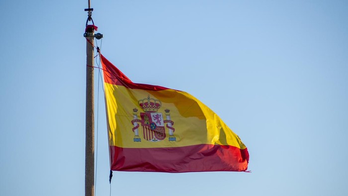 The national flag of Spain hung on the flagpole over a clear blue sky