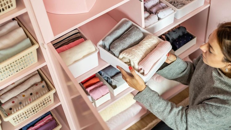 Happy young mother enjoying tidying up at female child wardrobe closet neatly folded clothes in plastic case box for comfortable vertical storage. Modern female cleanup kids cupboard Konmari method