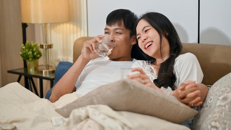 Ilustrasi suami istri A happy young Asian couple in pajamas is enjoying watching television or a movie together in bed. couple and domestic life concepts