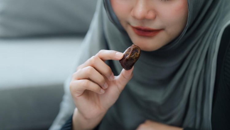 Muslim woman in hijab eating dates fruit in a comfortable home. Clouse up shot