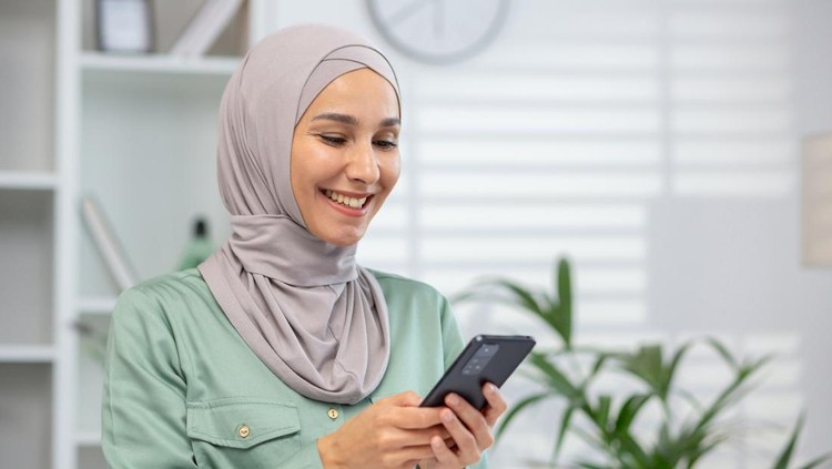Ilustrasi wanita hijab menggunakan ponsel Cheerful Muslim woman wearing a hijab engages with her smartphone, portraying connectivity and modern lifestyle.