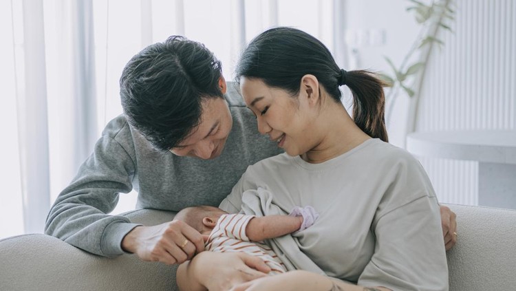 Asian Chinese young mother breastfeeding baby girl at home with father