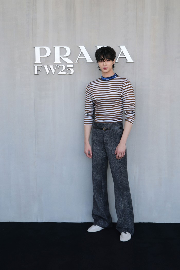 Maskulin tapi tetap modis. Byeon Wooseok memadukan dua motif garis, yakni kaus putih-coklat bermotif horizontal, sedangkan stripes lainnya pada loose pants abu-abu. Aksen biru menghias garis lehernya. Untuk mempertahankan kesan minimalis, aktor Korea Selatan ini mengombinasi outfit dengan sneakers putih/ Foto: Courtesy of Prada