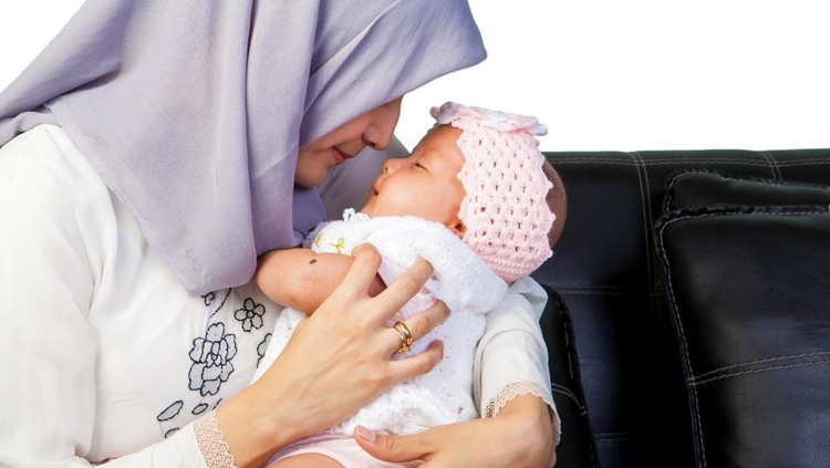 Portrait Adult muslim mother wearing traditional black dress and headscarf&comma; carrying little baby boy&comma; smiling with happiness in indoor home with copy space&period; Education&comma; Family&comma; Religious Concept