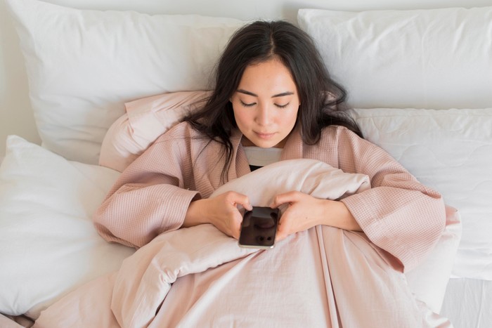 Ilustrasi perempuan sedang bermain ponsel sebelum tidur/Foto: Freepik.com/Freepik