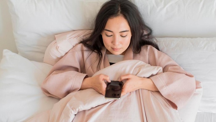 Ilustrasi perempuan sedang bermain ponsel sebelum tidur/Foto: Freepik.com/Freepik