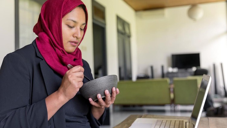 Portrait shot of modern Muslim woman eating her iftar meal alone, after finished work during lockdown Covid 19 at home