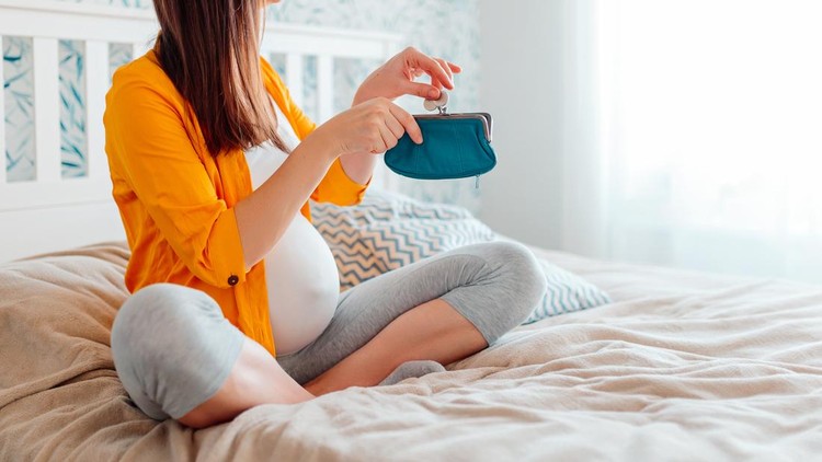Pregnant woman holding purse in bed. Pregnant woman counting money in purse, putting coins into purse.