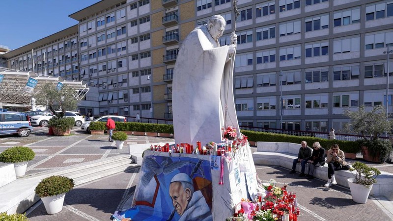 Orang-orang berdoa ke dekat patung mendiang Paus Yohanes Paulus II pada luar Rumah Sakit Gemelli tempat Paus Fransiskus dirawat, di Roma, Italia, 5 Maret 2025. (REUTERS/Remo Casilli)