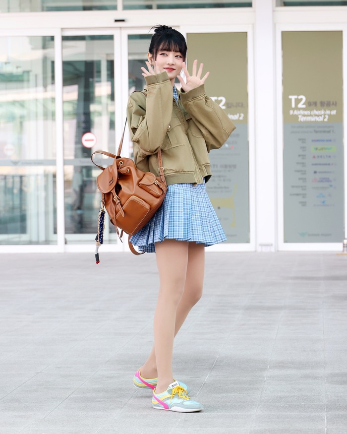 Penampilan Minnie nggak kalah menarik! Jaket bernuansa utilitarian dipasangkan dengan mini dress plaid biru dengan rok lipit. Gayanya makin serupa anak sekolah dengan ransel coklat berhias bag charm, tatanan rambut messy bun, dan sneakers multi warna/ Foto: Dok. Miu Miu
