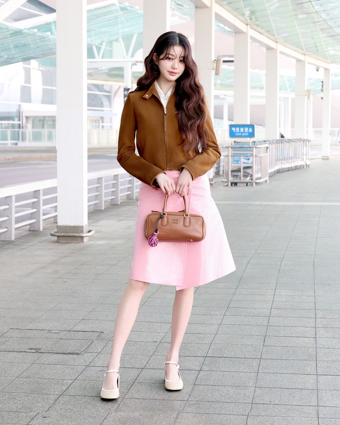 Dengan jaket coklat minimalis yang senada tas Arcadie, Wonyoung Jang tampil manis, Beauties! Jaket tersebut dipadu rok selutut asimetris warna pink dan sepatu mary jane krem yang lembut. Sementara itu, blus putih mengintip dari balik jaketnya/ Foto: Dok. Miu Miu