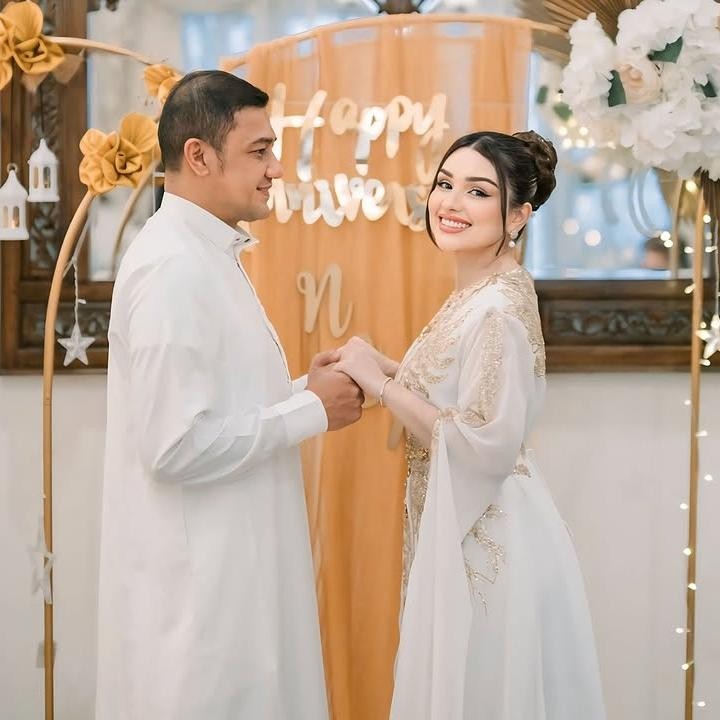<p>Dalam foto yang dibagikan, Teuku Rafly dan Nourah Sheivirah terlihat kompak mengenakan pakaian berwarna putih. Keduanya berdiri di depan <em>backdrop</em> yang dihiasi balon berwarna emas dan putih. Di tengahnya juga terdapat kain berwarna jingga yang bertuliskan 'Happy Anniversary' dan inisial nama mereka. (Foto: Instagram @nourahsheivirah)</p>