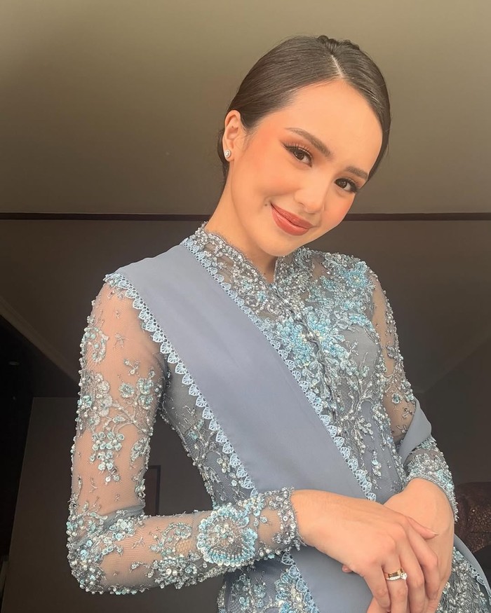 Bebby Tsabina elegan mengenakan kebaya biru brokat dengan payet senada. Selendang abu-abu dengan pinggiran renda lembut tersampir di pundak. Mengimbangi busana formal tersebut, cincin dan subeng berlian disematkan serta rambut tersanggul rapi./ Foto: Instagram.com/bebytsabina