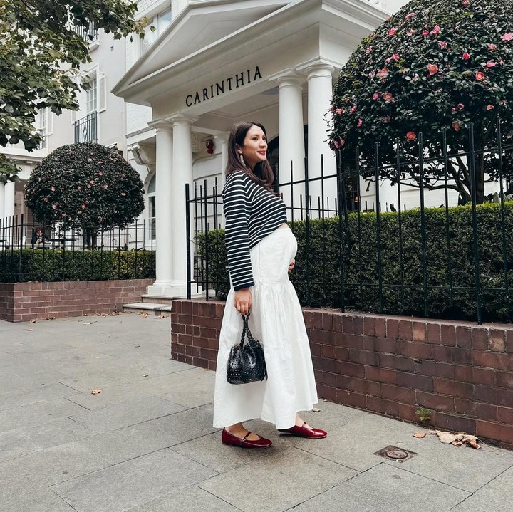 <p>Di foto lainnya, Acha memamerkan <em>baby bump</em> kehamilannya yang dibalut dengan rok putih panjang dengan kaos bergaris. Untuk menyempurnakan penampilannya yang simpel, Acha mengenakan sepatu tanpa hak berawarna merah dan tas hitam kecil. (Foto: Instagram @achasinaga)</p>