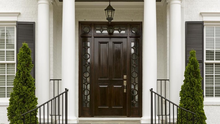 A grand entrance way leading up to an ornate dark wood door with green trees.