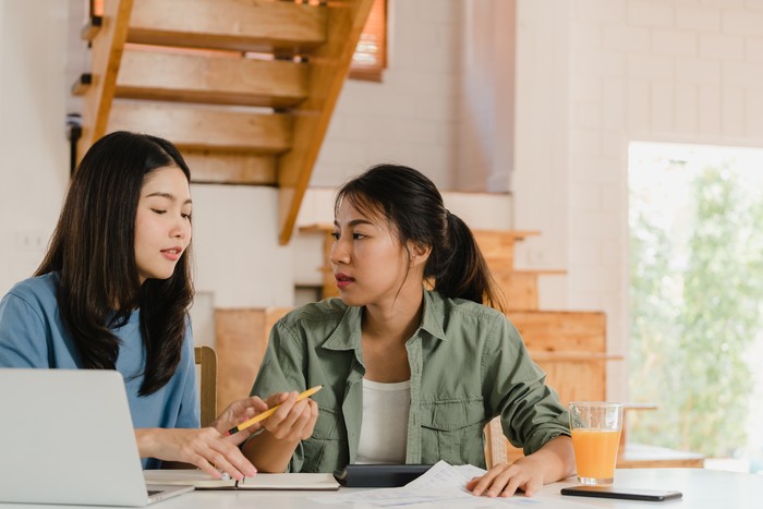 Business Asian Lesbian lgbtq women couple do account at home, Young Asia girl serious, stress while using calculator record budget, tax, financial document on laptop working in kitchen concept.