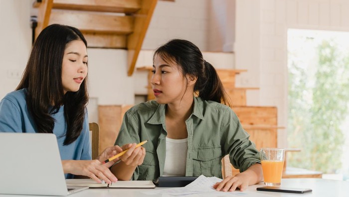 Business Asian Lesbian lgbtq women couple do account at home, Young Asia girl serious, stress while using calculator record budget, tax, financial document on laptop working in kitchen concept.