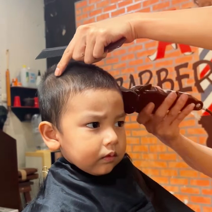 <p>Selama dicukur, Naka terlihat anteng dan tidak rewel. Ia juga sangat serius memerhatikan gerak-gerik sang tukang cukur yang merapikan rambutnya. (Foto: Instagram: @indahpermatas)</p>
