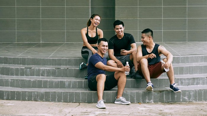 Laughing friends sitting outdoors, laughing and chatting after training