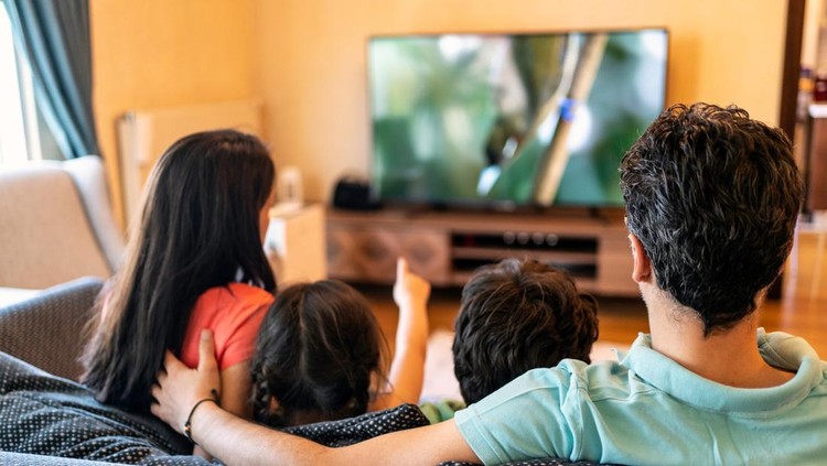 Parents and their two children watching TV together at home