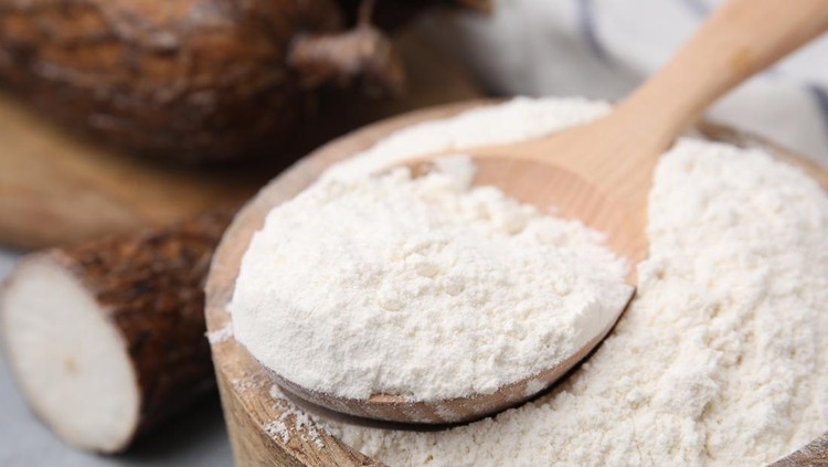 Wooden bowl and spoon with cassava flour on table, closeup