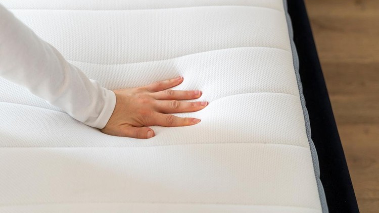 Cropped shot of woman hand testing new orthopedic memory foam core mattress at comfortable bed at home&period; Female customer choosing equipment for healthy sleeping