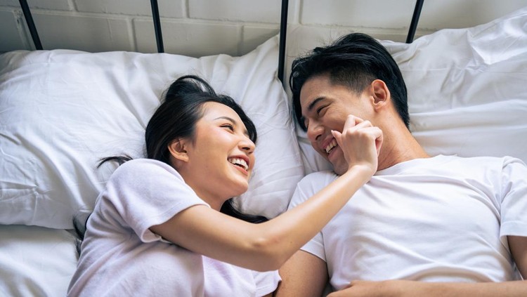 Ilustrasi pillow talk Asian new marriage couple lying down on bed and looking at each other. Attractive beautiful young man and woman in pajamas enjoy early morning activity in bedroom at home. Family relationship concept