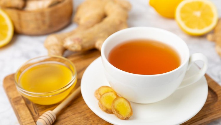 Ilustrasi resep minuman herbal jahe Cup of hot ginger tea with slices of ginger root on wooden background. Warming drink. Alternative medicine. Tea with honey, lemon, ginger and mint. Space for text. Copy space