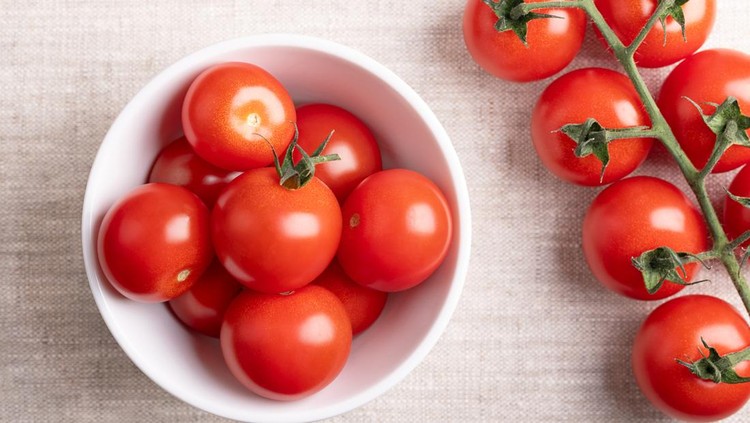 Red cherry tomatoes in a white bowl on linen fabric&period; Fresh&comma; ripe type of small and round cocktail tomatoes&comma; on the left side still on the vine&comma; from above&period; Solanum lycopersicum var&period; cerasiforme&period; Photo