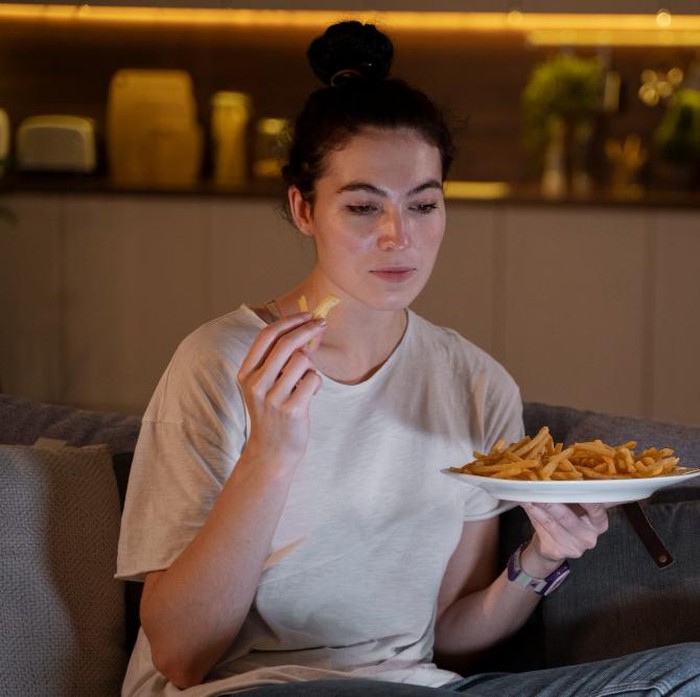 Ilustrasi perempuan sedang makan sambil menonton televisi/ Foto: Freepik