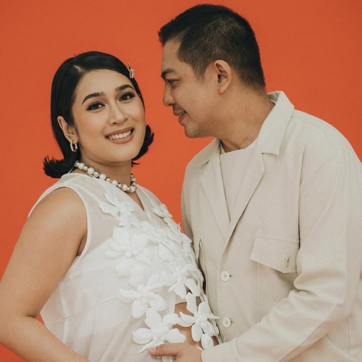 <p>Tampak pada foto keduanya tampak bahagia berpose dengan latar belakang oranye dan busana serba putih. Indi tampak cantik mengenakan setelan celana san atasan bunga putih, sedangkan Ade mengenakan outer jaket yang kasual. "Menghitung harinya bundi @indiarisa_ menuju hari lahir buah hati kami tercinta untuk hadir di dunia ini," tulis Ade. Foto: Instagram @adegovinda</p>