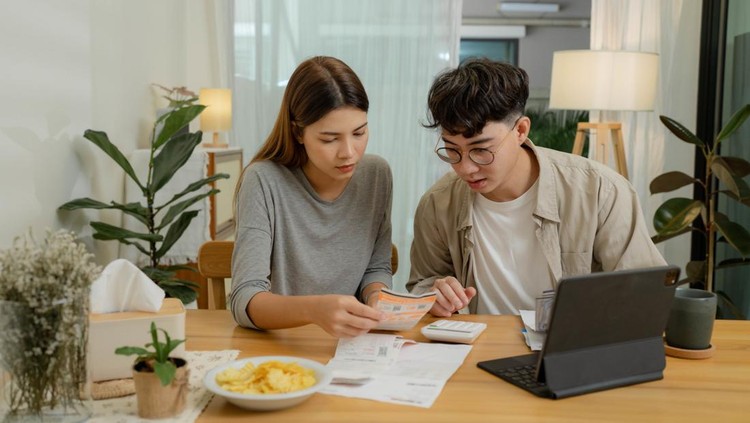 Ilustrasi pasangan merencanakan keuangan Happy young couple using laptop pay bills online in app calculate investment payment budget discuss finances at home.