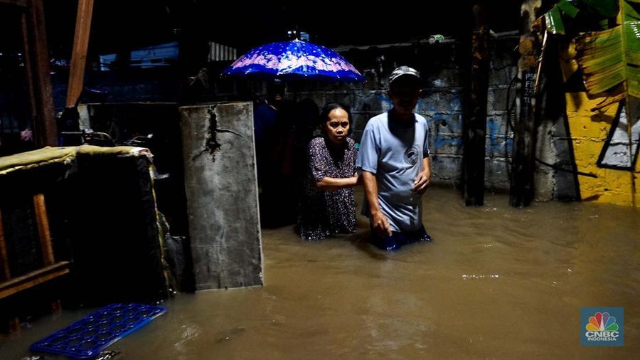 Sejumlah penduduk melintas di tengah banjir di RW 06 Jatipadang, Jakarta Selatan, (6/7/2025). (librosfullgratis.com/Muhammad Sabki)
