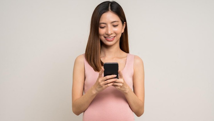 ibu hamil dan ponsel Happy Pregnant asian woman stroking touch belly motherhood with smartphone application on isolated background. Family planning maternity and pregnancy with insurance for child health technology.