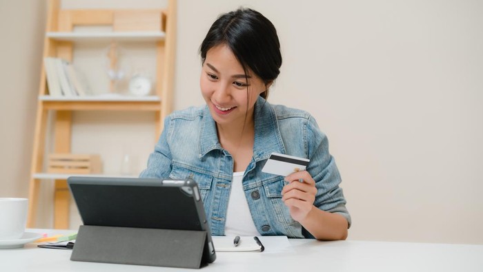 Beautiful smart business Asian woman using tablet buying online shopping by credit card while wear smart casual sitting on desk in living room at home. Lifestyle woman working at home concept.