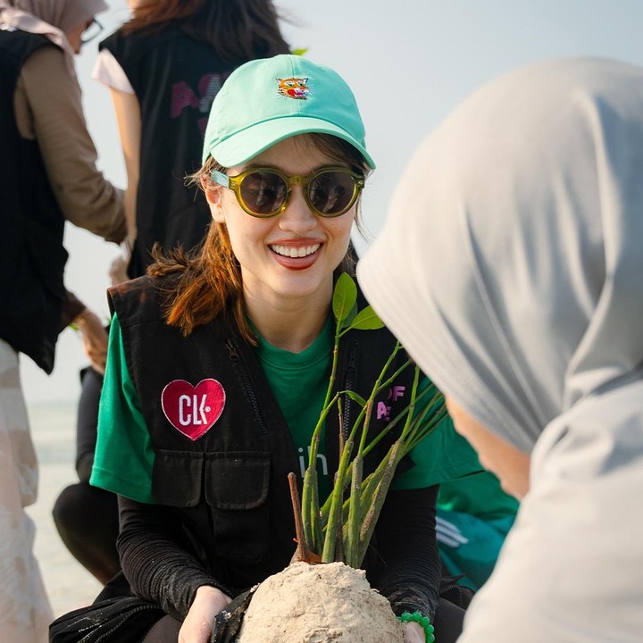 <p>Saat menanam mangrove, Cinta terlihat mengenakan pakaian santai namun berwarna senada. Ia tampak memakai kaus dan topi hijau, yang dipadukan kaus manset, jaket rompi, serta celana hitam. Perempuan 31 tahun ini juga terlihat mengenakan aksesoris gelang hijau dan kacamata hitam. (Foto: Instagram @claurakiehl)</p>