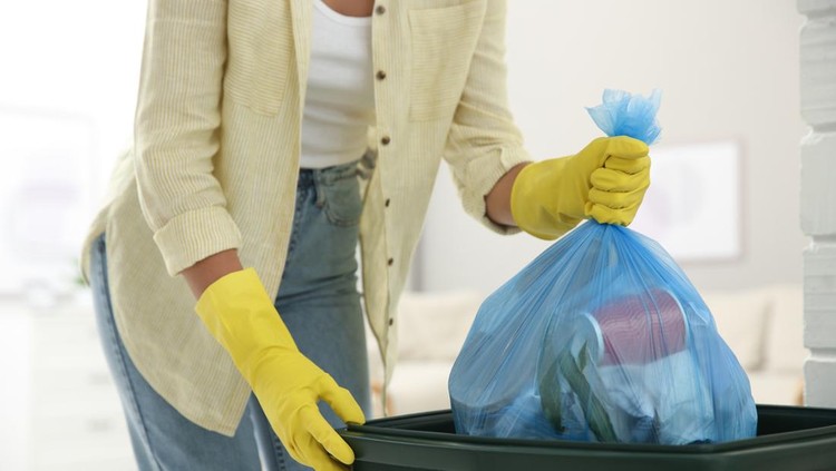 Woman throwing garbage bag into bin at home, closeup