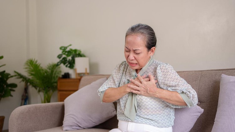 Asian senile woman with body aches, leg pain, chest pain, muscle stiffness, arm pain, hand pain, sitting on a sofa in the living room stretching.