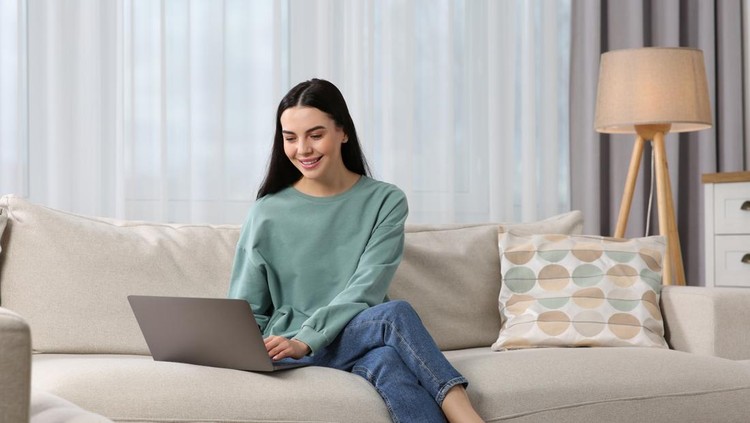 Happy woman working with laptop on sofa at home