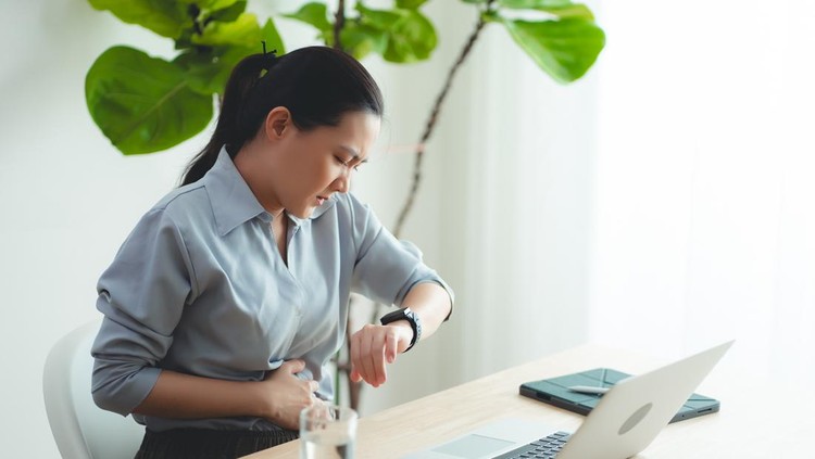 Asian woman feeling stomachache and touching her belly sitting at home office.
