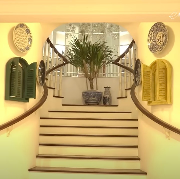 <p>Salah satu sudut yang disukai Yuni adalah tangga di dalam rumahnya. Tangga yang didesain melingkar oleh arsitek ini dibuat begitu <em>aesthetic</em> dengan banyak hiasan piring di kanan dan kiri dinding. Area tangga ini menjadi lokasi pilihan Yuni saat ingin mengabadikan momen foto pribadi atau bersama keluarga. (Foto: YouTube Melaney Ricardo)</p>