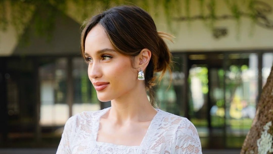Cinta Laura mengenakan kebaya putih dengan aksen selendang merah di pinggang.