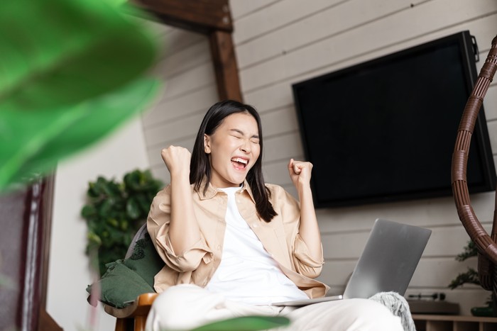 Joyful asian woman winning online on laptop, celebrating victory, shouting and rejoicing, triumphing.