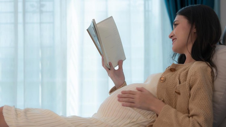 Pregnant woman reading a stories to her unborn child in the living room at home