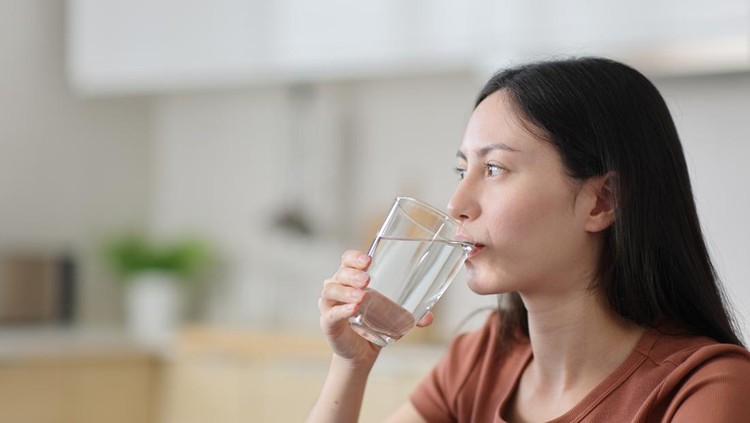 Ilustrasi haus atau minum air Asian woman drinking tap water from glass in the kitchen